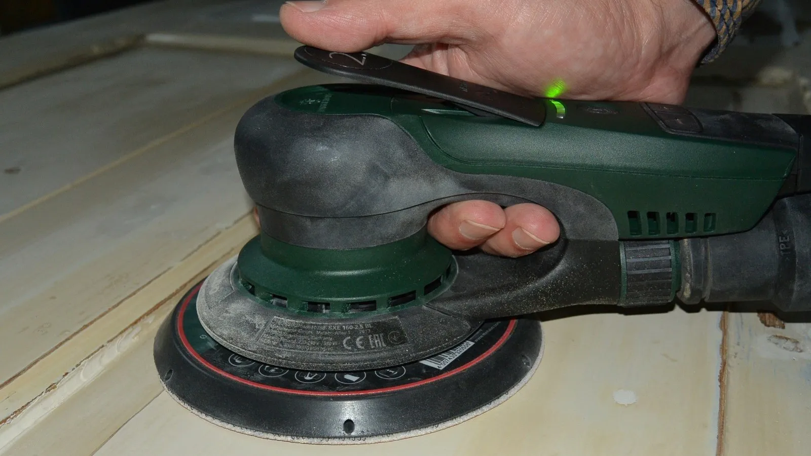 Eine Hand hält den Metabo Exzenterschleifer an eine Oberfläche.